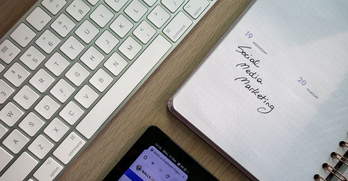 Top view of a keyboard, planner with a social media marketing note, and tablet, representing the best tool to schedule social media posts