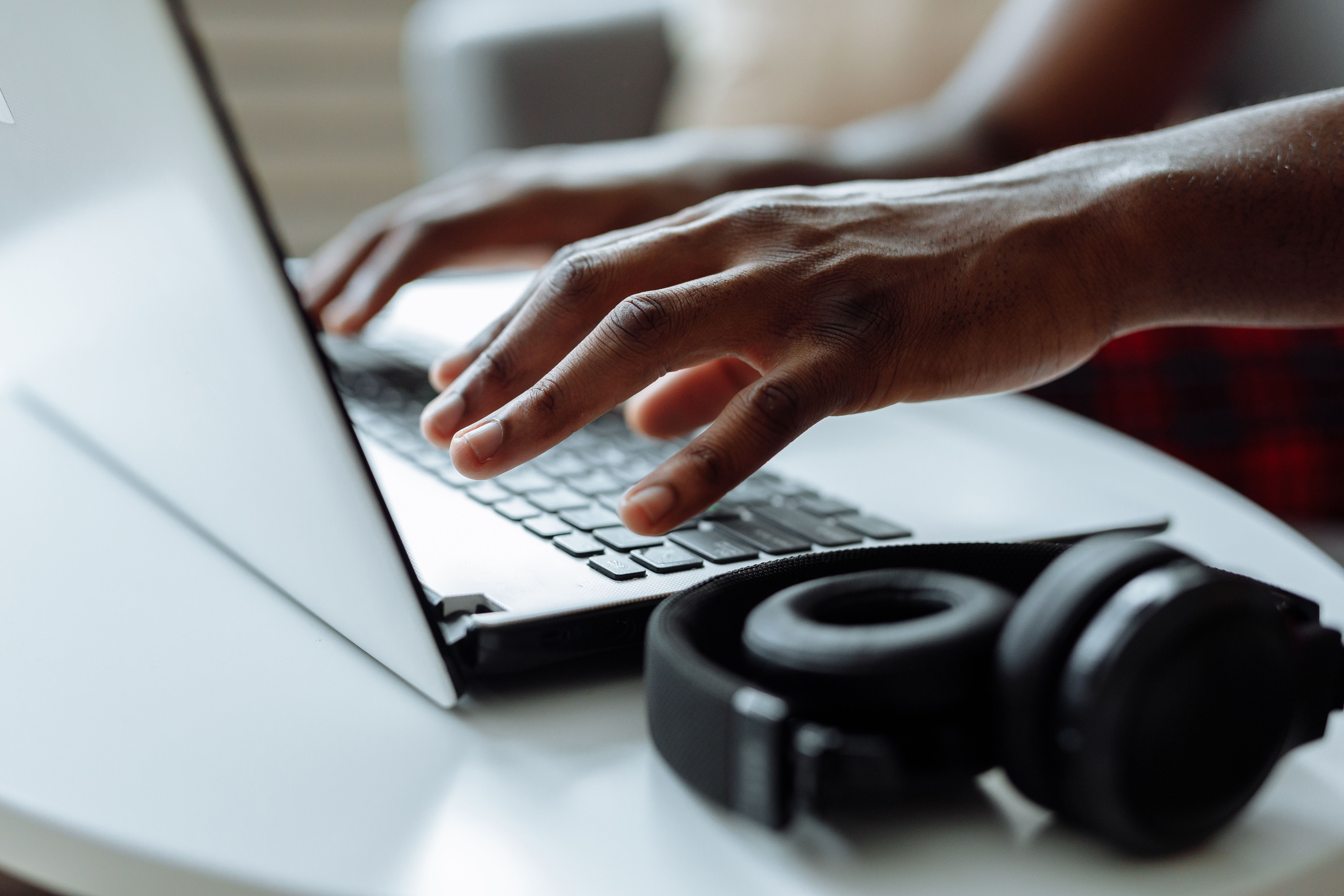 Faceless content creator typing on a laptop beside headphones, face not shown