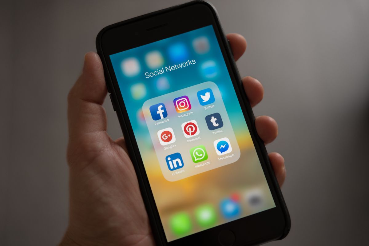 Person holding a phone showing Instagram and other social media apps while writing an Instagram caption