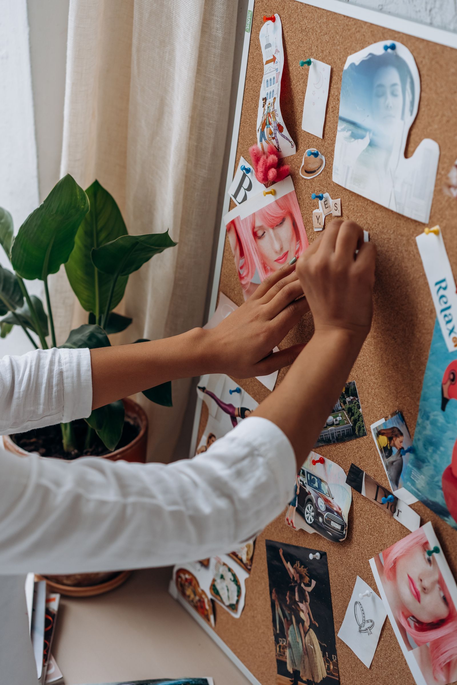 Hand pinning photos and notes to a board, planning Pinterest pins on a schedule