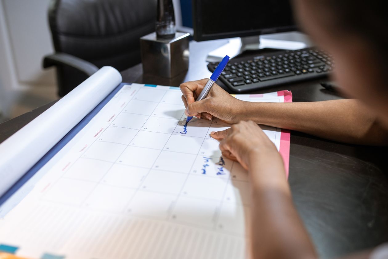 Person planning a social media content calendar on a desk calendar next to a laptop